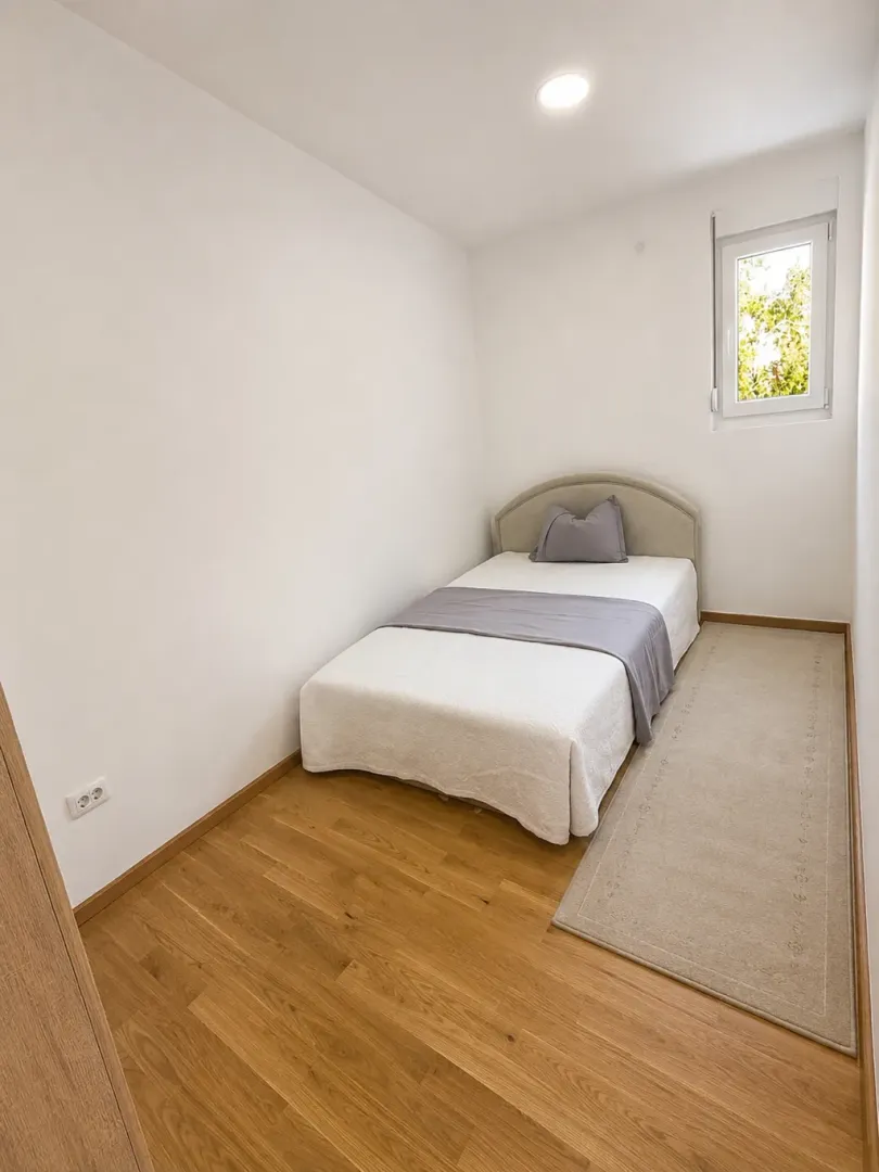 Jednostavna spavaća soba sa jednim krevetom i svijetlim zidovima.
