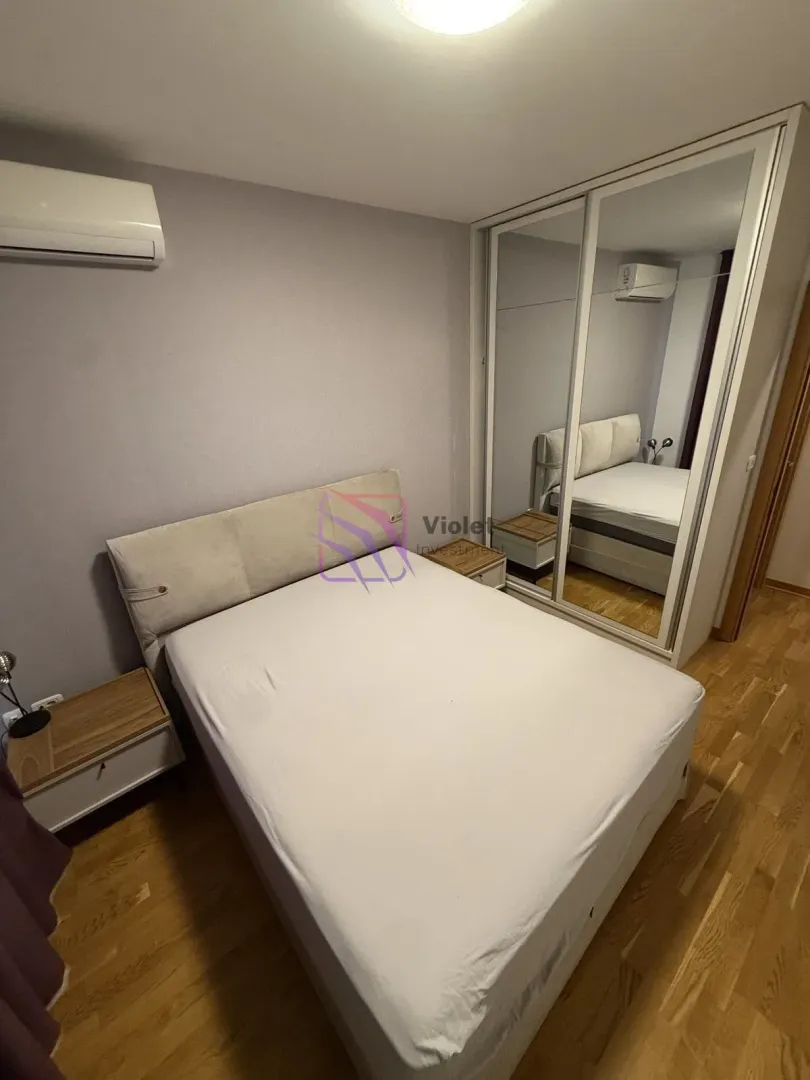 Namještena spavaća soba sa bračnim krevetom, noćnim stočićima i velikim garderoberom sa ogledalom.