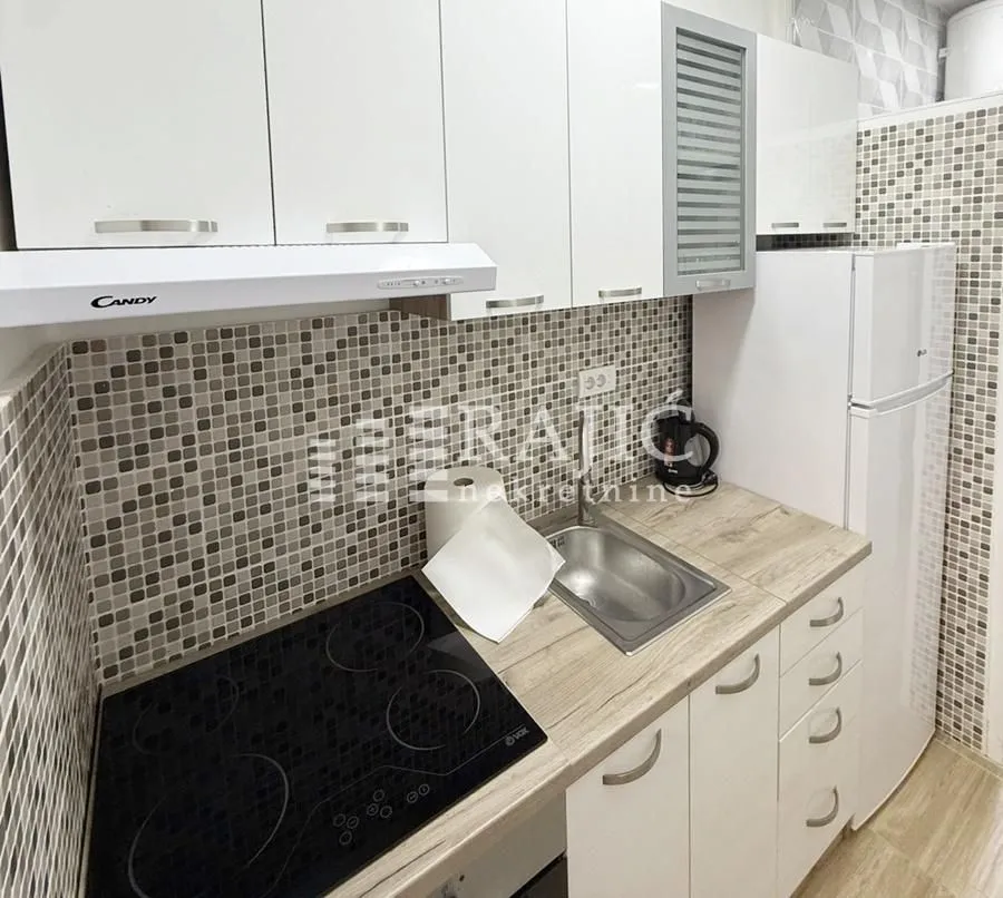 Small kitchen with white cabinets, built-in cooktop, and a refrigerator.