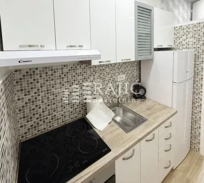 Small kitchen with white cabinets, built-in cooktop, and a refrigerator. - image 4