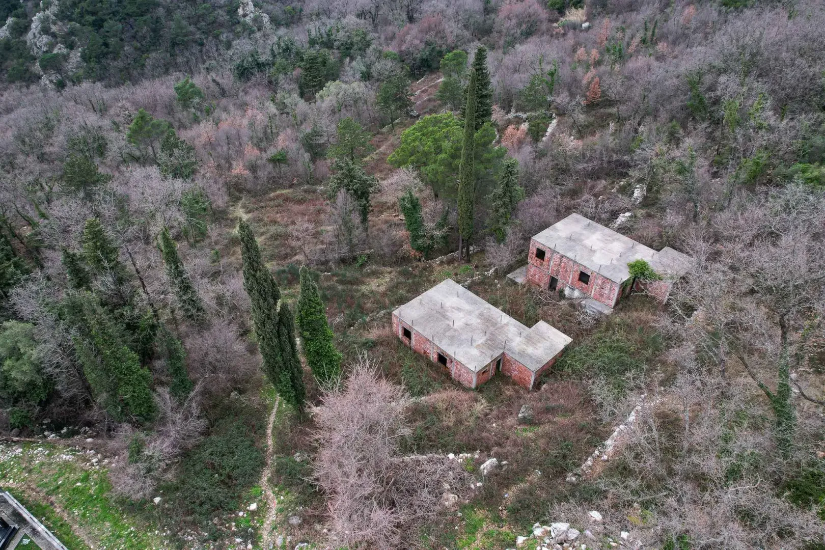Pogled iz vazduha na dvije nezavršene kuće u šumovitom okruženju.