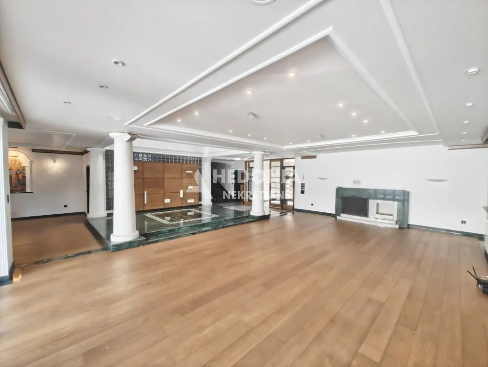 Spacious living room with wooden flooring, pillars, and a dropped ceiling with lighting.