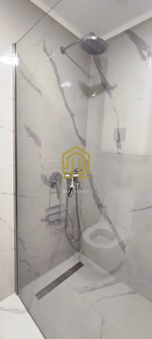 Moderno opremljeno kupatilo sa tuš kabinom i mermernim pločicama.