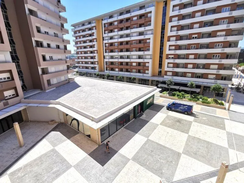 Pogled s visine na popločano dvorište i moderne stambene zgrade.