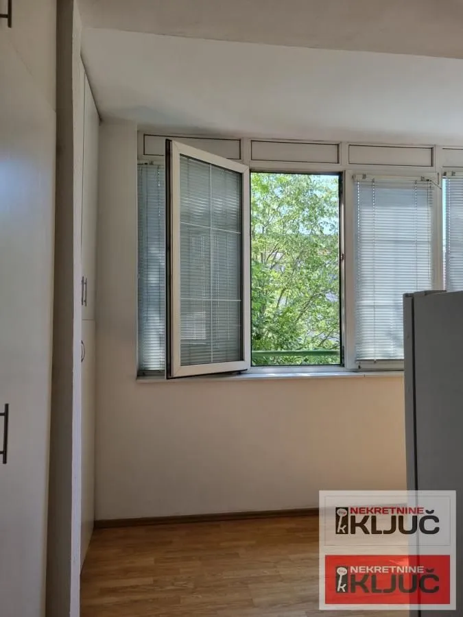 Pogled kroz otvoreni prozor na zelenilo i drveće.