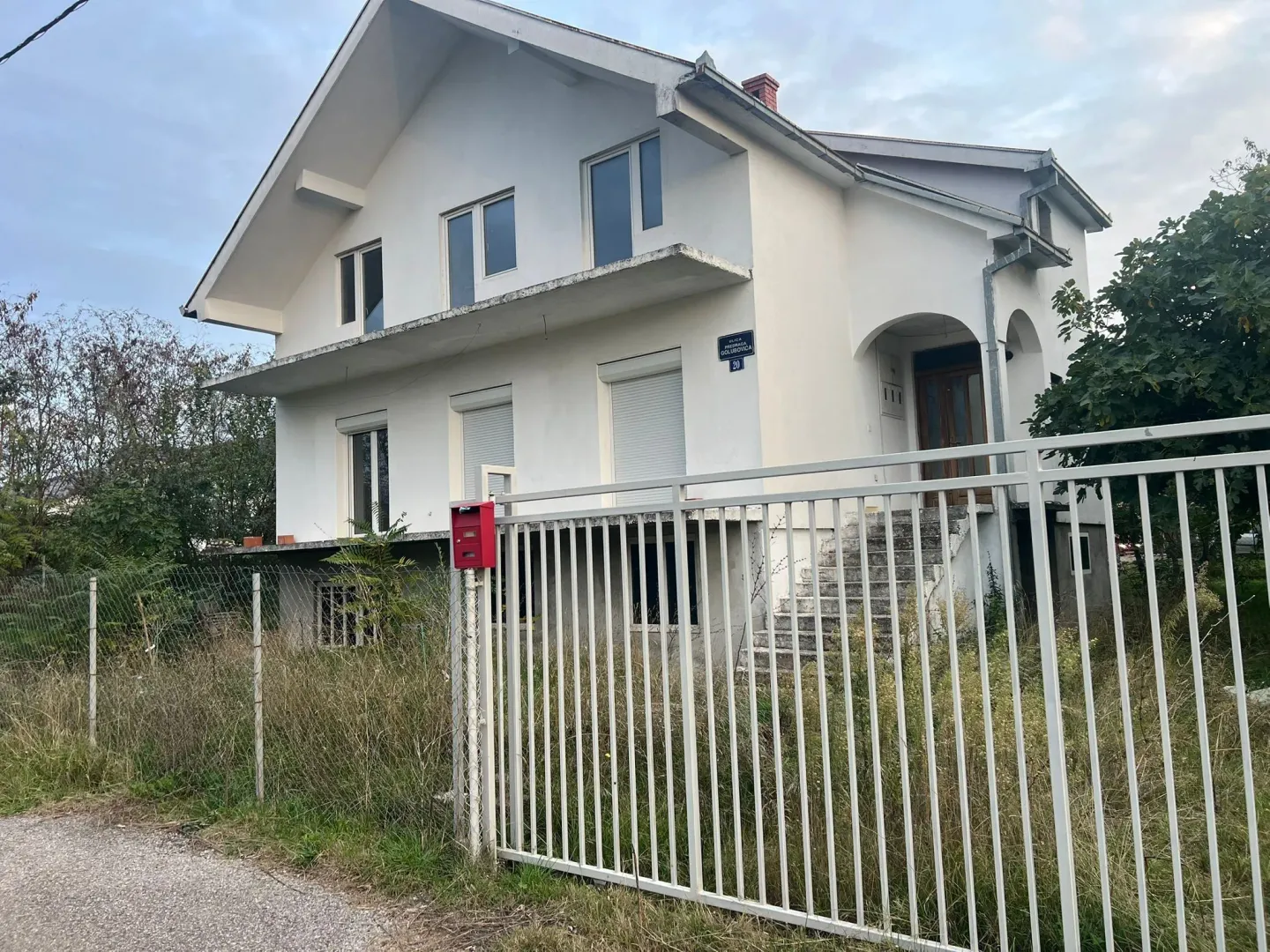 Dvospratna bijela kuća sa ogradom.