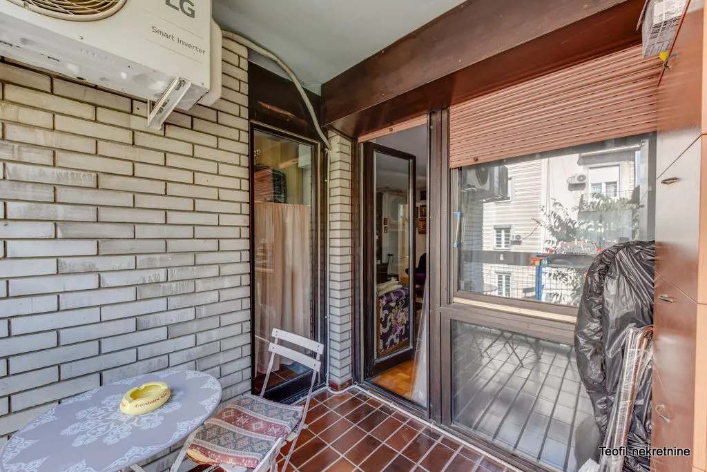 Covered balcony with a table, chairs, and an outdoor air conditioning unit.
