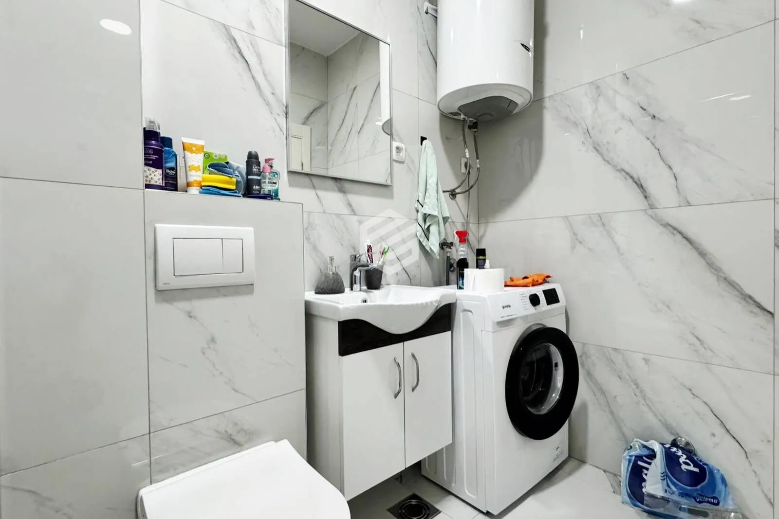 Modern tiled bathroom with a washbasin, mirror, toilet and washing machine.