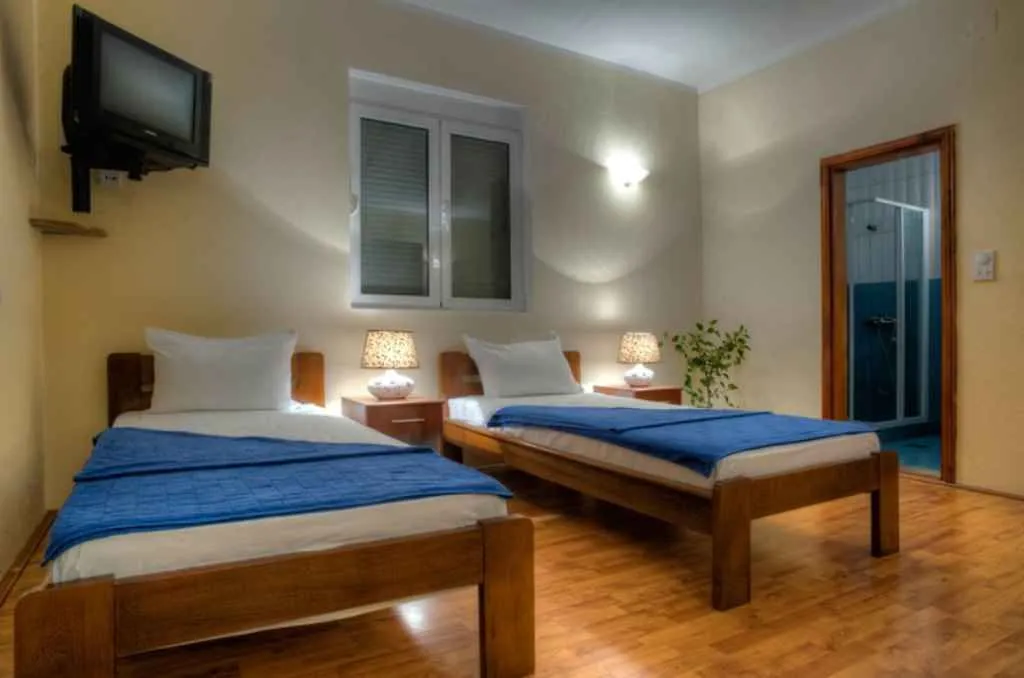 Spavaća soba sa dva singl kreveta, noćnim stočićima i televizorom na zidu.