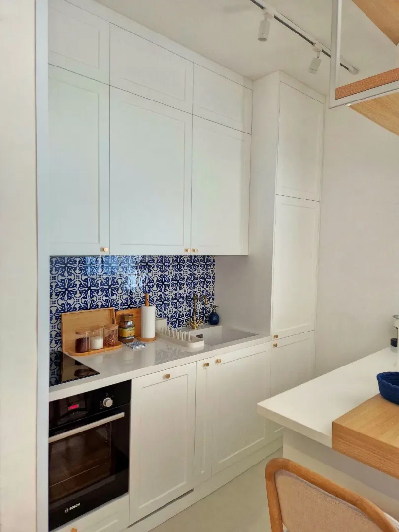 Modern white kitchen with decorative tiles and built-in appliances.