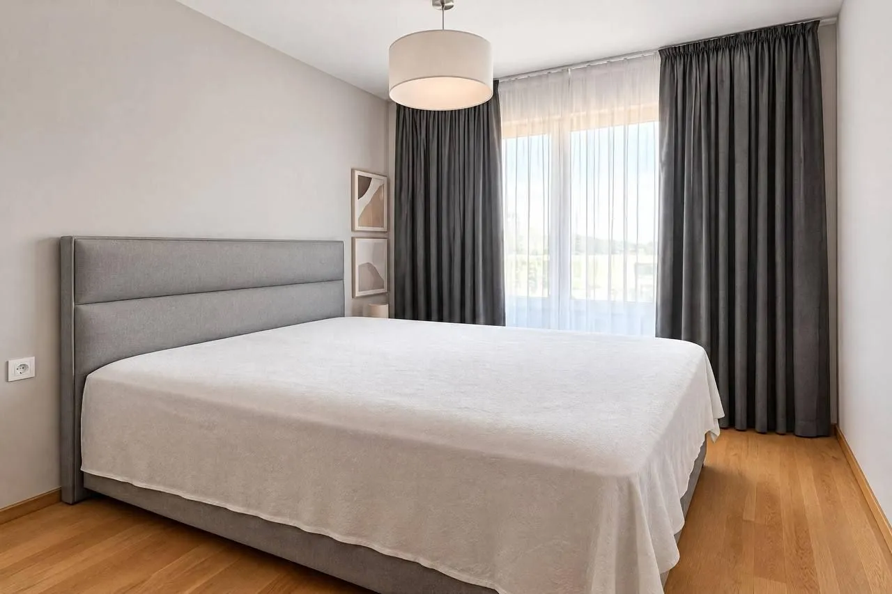 Modern bedroom with a large double bed and dark curtains.