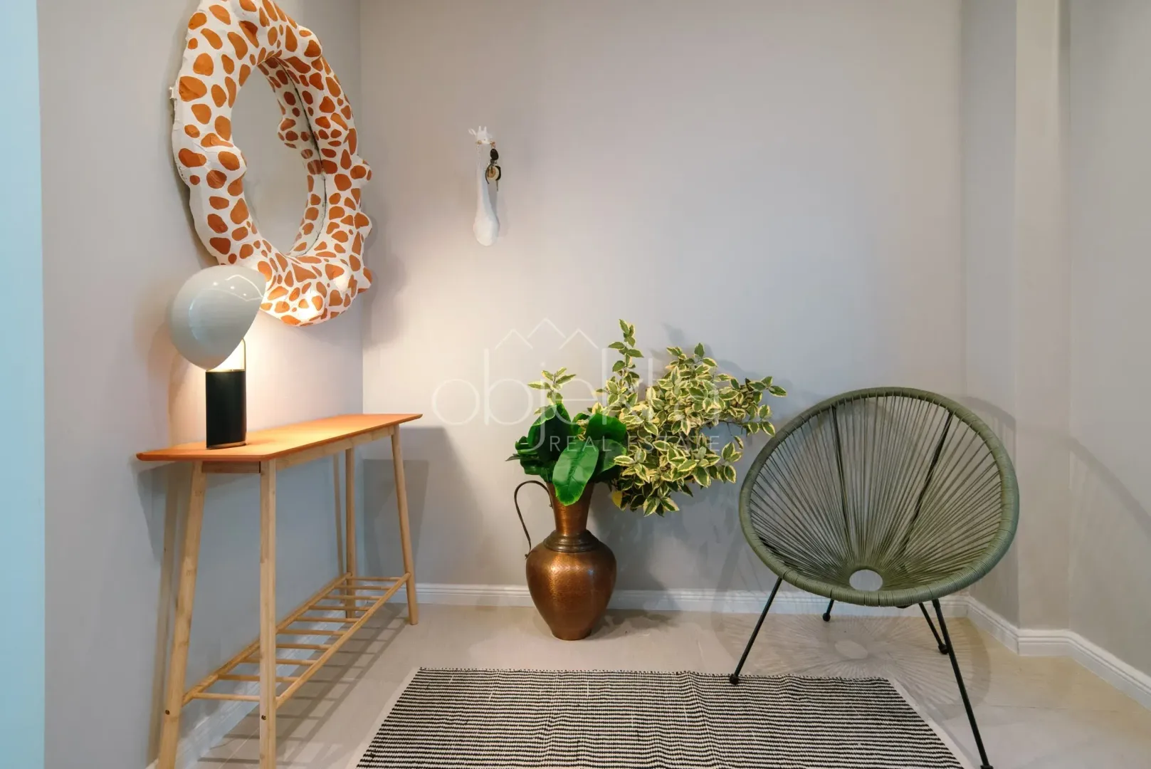 Ugao dnevne sobe sa ukrasnim ogledalom, stočićem, vazom sa biljkama i zelenom foteljom.