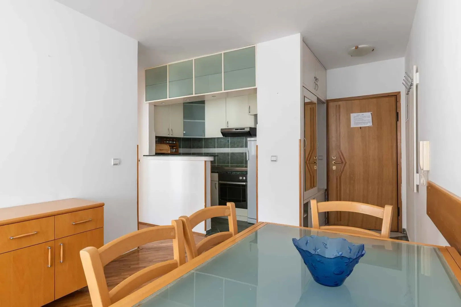 Dining area with a view of the small kitchen and entrance door.