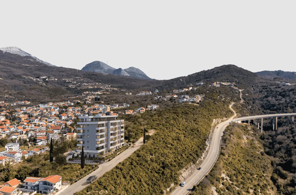 Pogled iz vazduha na novu stambenu zgradu sa okolinom i planinskim pejzažom.
