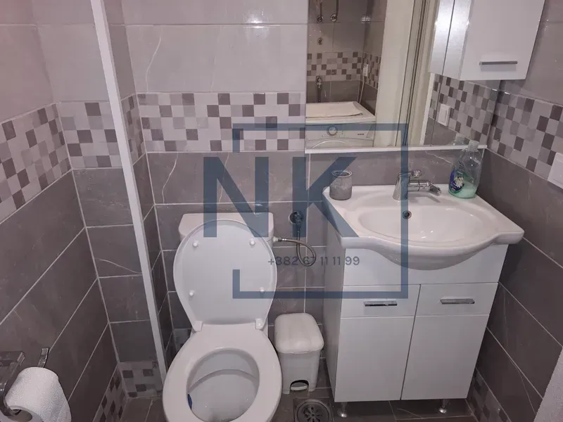 Small bathroom with a washbasin, toilet bowl and grey tiles.