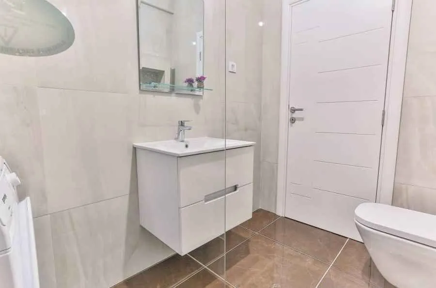 Moderne kupatilo opremljeno umivaonikom, ogledalom i wc šoljom.
