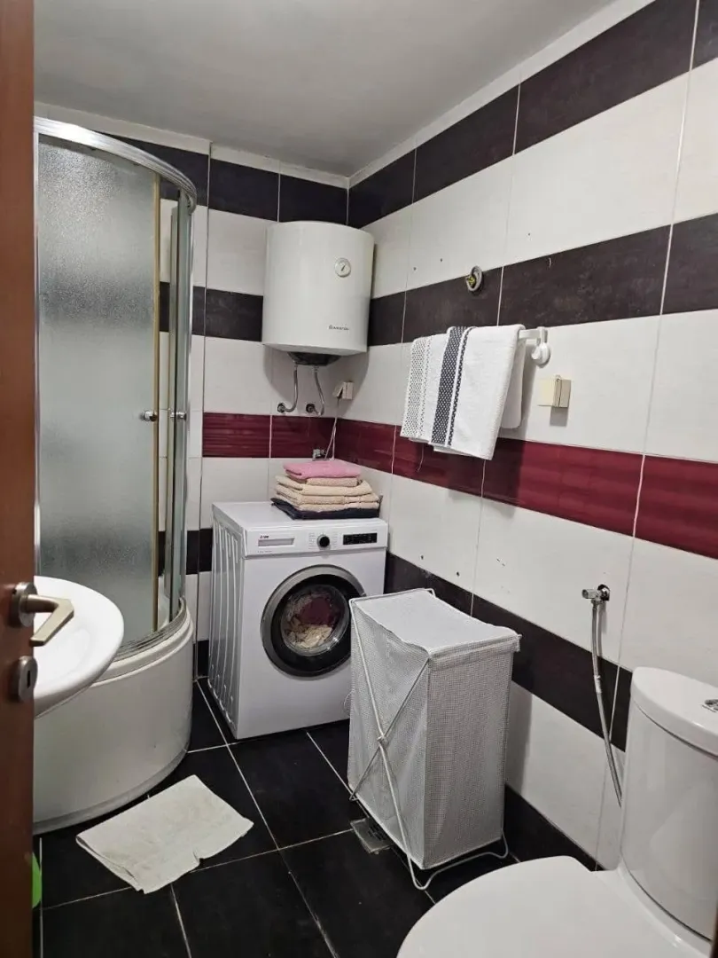 Small bathroom with a shower cabin, washing machine, and white and red tiles.