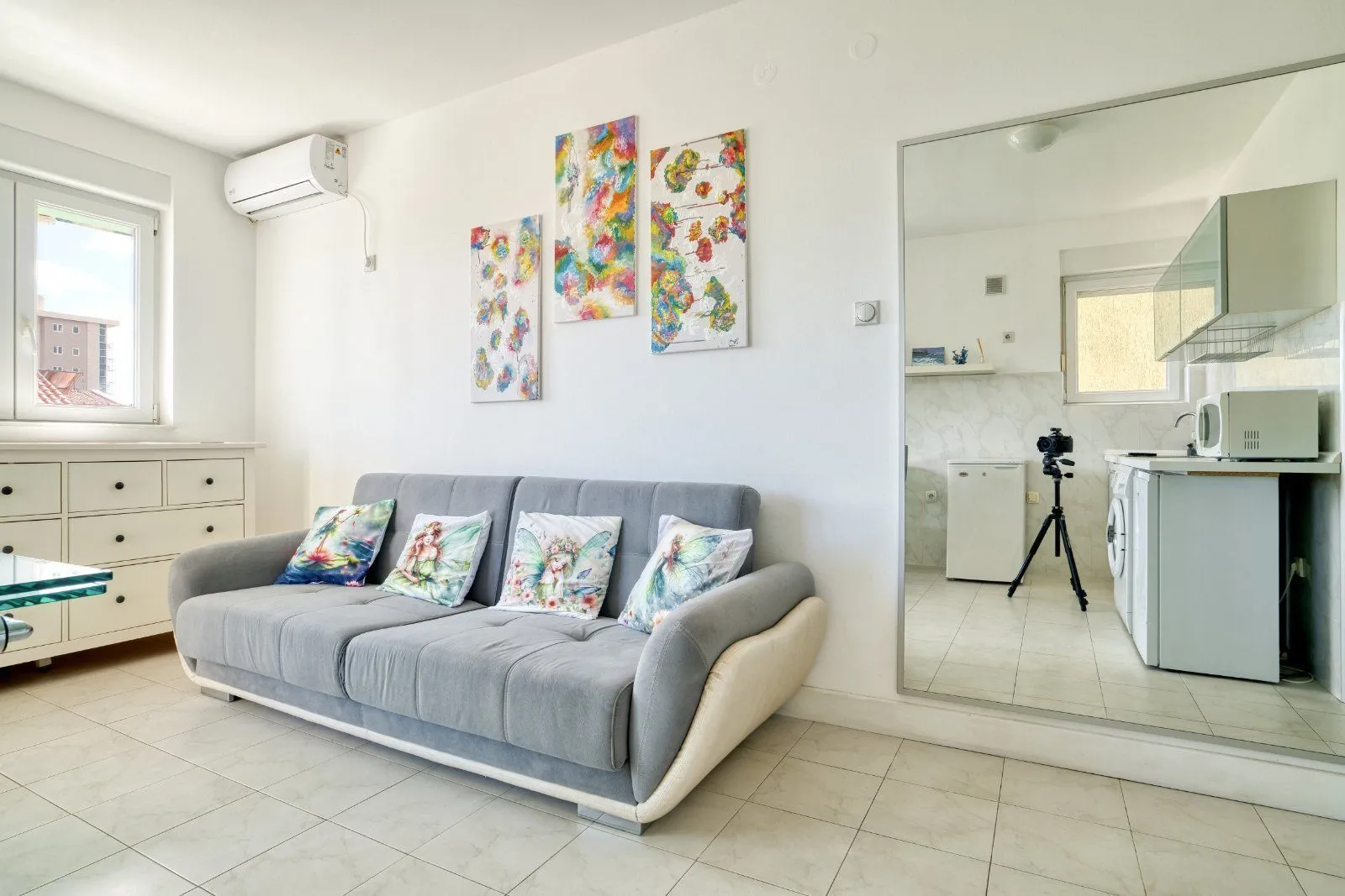 Living room with a grey sofa, decorative paintings, and an air conditioner.
