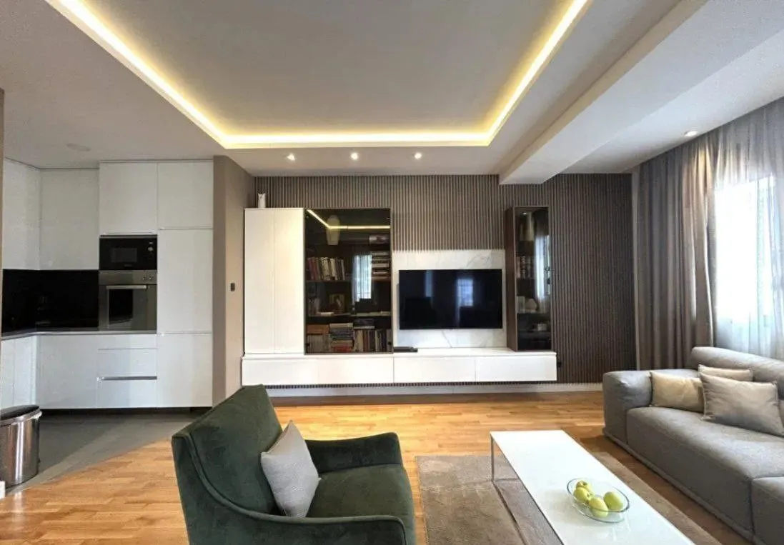 Modern living room connected with the kitchen, equipped with a sofa, TV unit, and built-in elements.