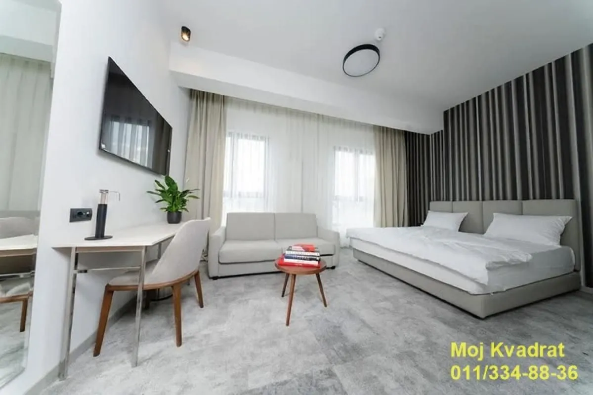 Modern bedroom with a double bed, sofa, desk, and television.