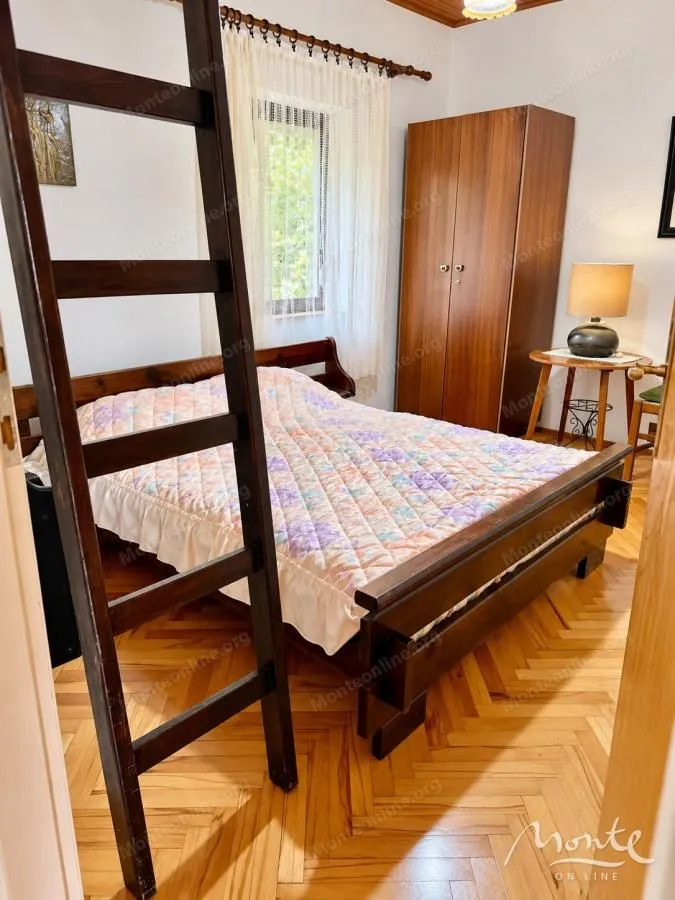 Namještena spavaća soba sa bračnim krevetom, ormarom i drvenim podom.