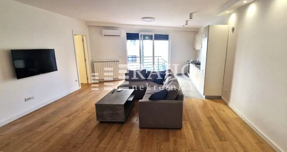 Spacious living room connected to the kitchen, featuring a sofa set and hardwood flooring.