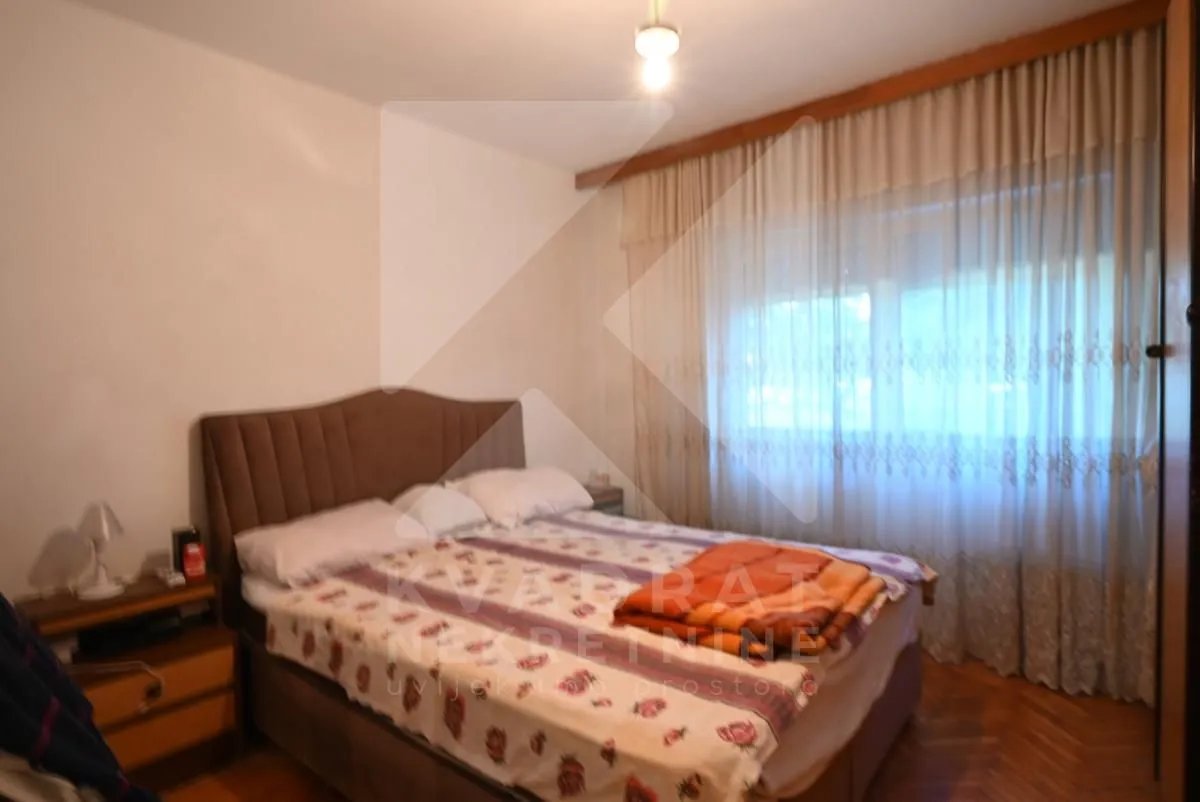 Spavaća soba sa bračnim krevetom i prozorom sa zavjesama.