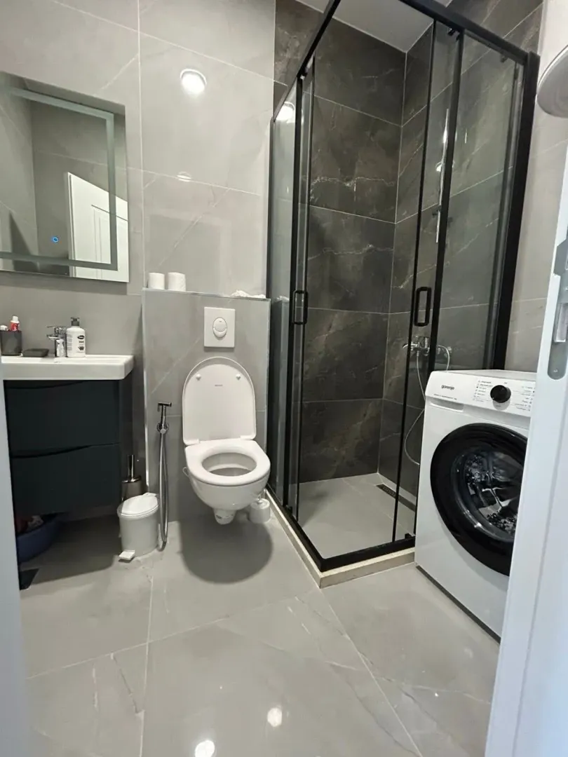 Moderne kupatilo sa tuš kabinom, umivaonikom i veš mašinom.
