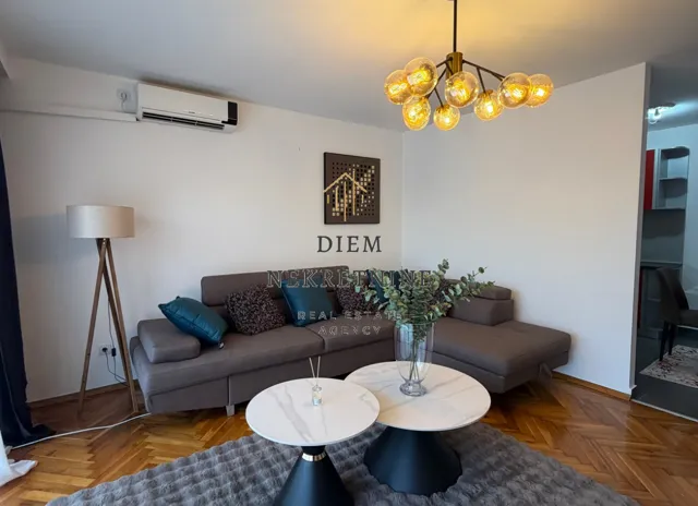 Dnevna soba sa ugaonom garniturom, stočićem i modernim lusterom.