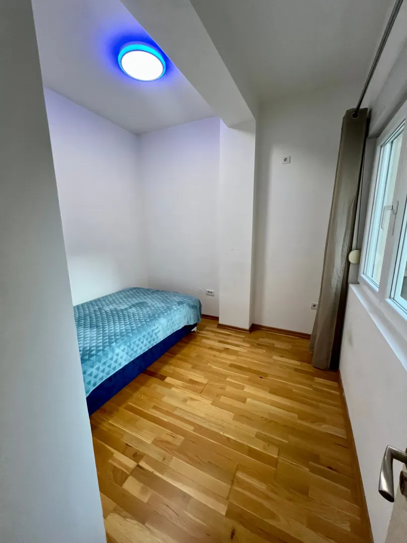 Small bedroom with a bed, wooden flooring, and a window.