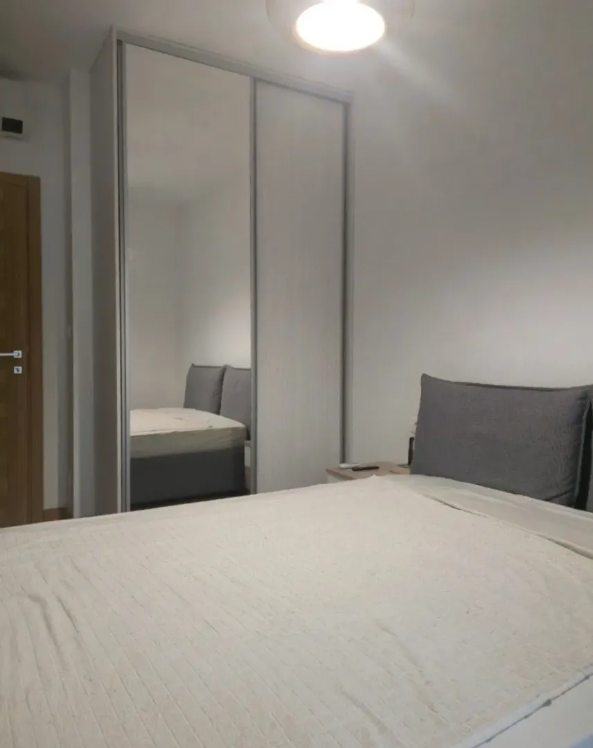 Moderna spavaća soba sa bračnim krevetom i velikim plakarom sa ogledalom.