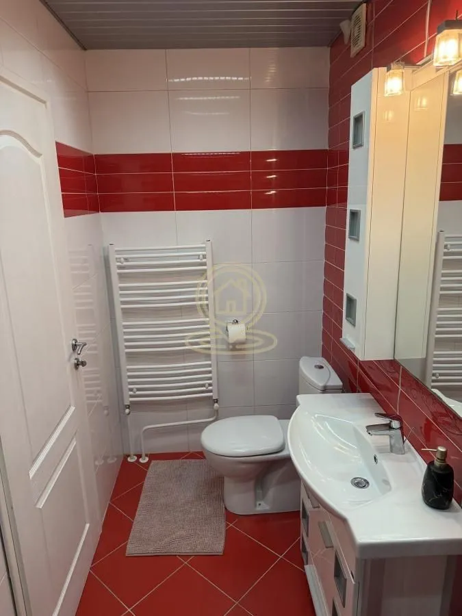Kupatilo sa belim i crvenim pločicama, umivaonikom i toaletom.