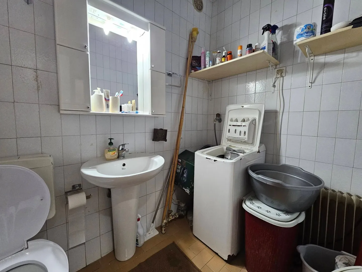 Small equipped bathroom with a sink, washing machine, and toilet.