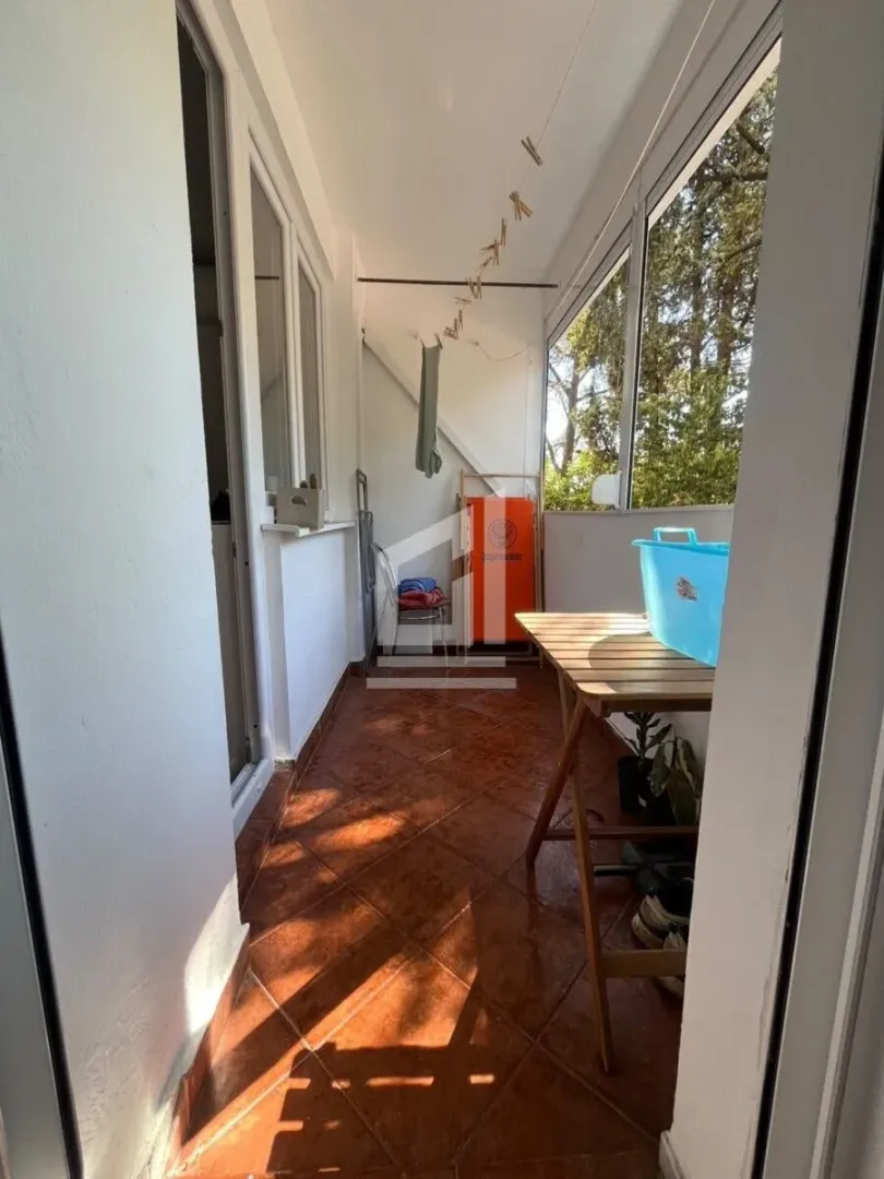 Zastakljeni balkon sa podnim pločicama i drvenim stolom.