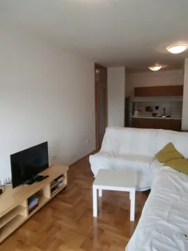 Living room with a sofa, television, and a view of the kitchen in the background. - image 7