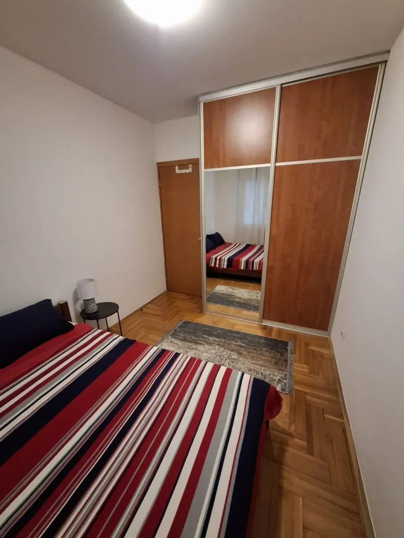 Jednostavna spavaća soba sa velikim ugradnim plakarom i drvenim parketom.