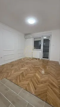 Prazna soba sa drvenim parketom, zidnim lajsnama, klima uređajem i izlazom na terasu. - image 3