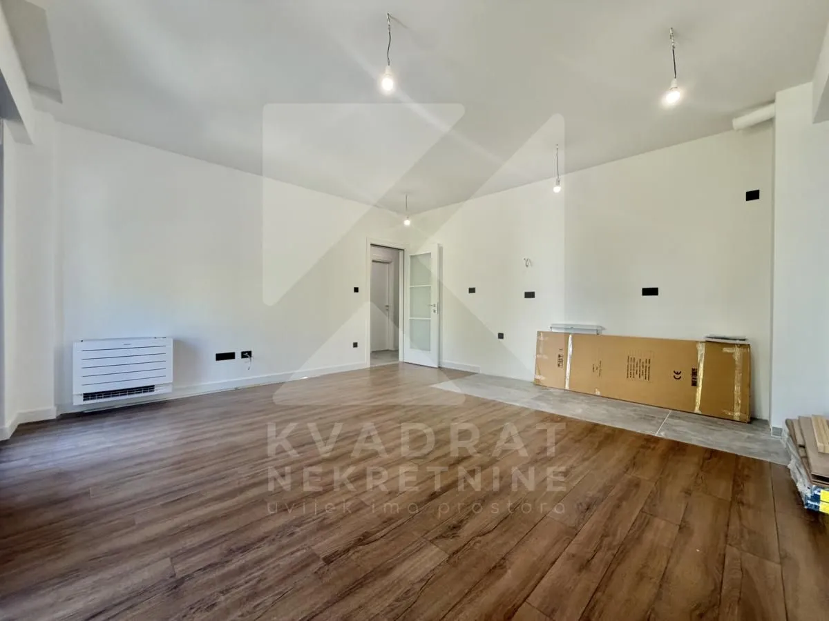 Empty room with wooden flooring, white walls and an air conditioning unit.