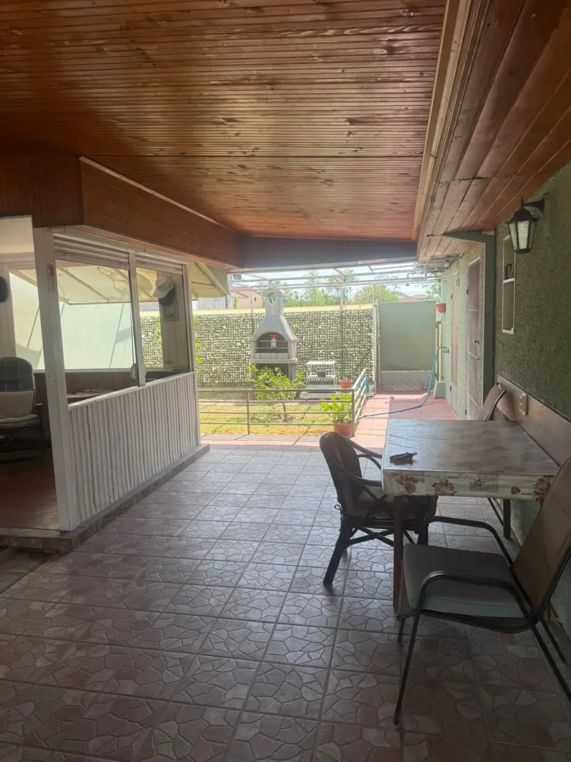 Natkrivena terasa sa stolom, stolicama i pogledom na dvorište sa roštiljem.