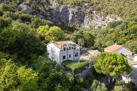 Pogled iz vazduha na kamenu kuću okruženu zelenilom i stenovitim brdom. - image 10