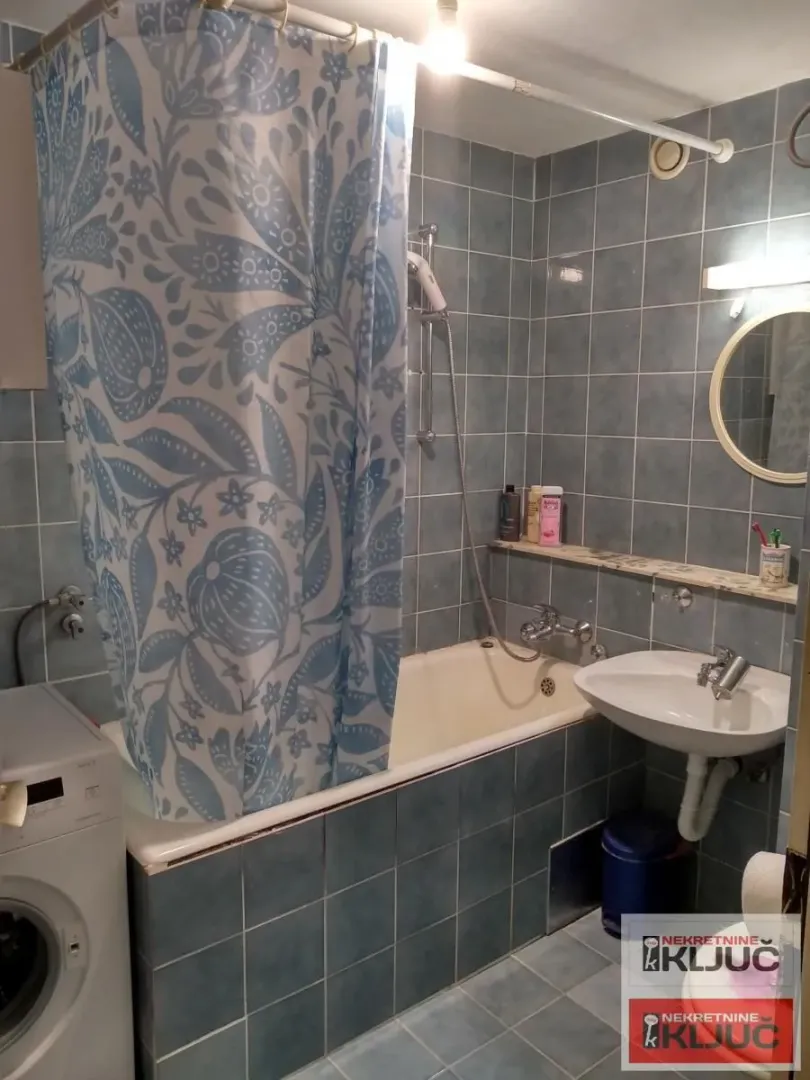 Kupatilo obloženo pločicama sa kadom, umivaonikom i veš mašinom.