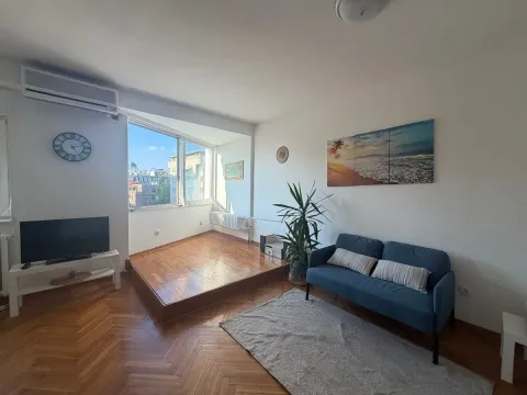 Dnevna soba sa plavim trosedom, televizorom i izdignutim drvenim podijumom kod prozora. - image 5