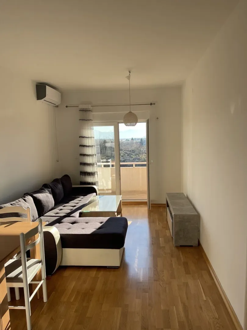 Svijetla dnevna soba sa ugaonom garniturom i izlazom na balkon.