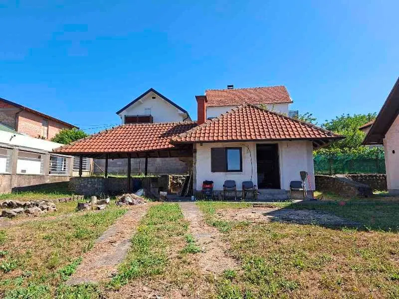 Pogled na dvorište i spoljašnjost kuće sa krovom od crepa i nadstrešnicom.