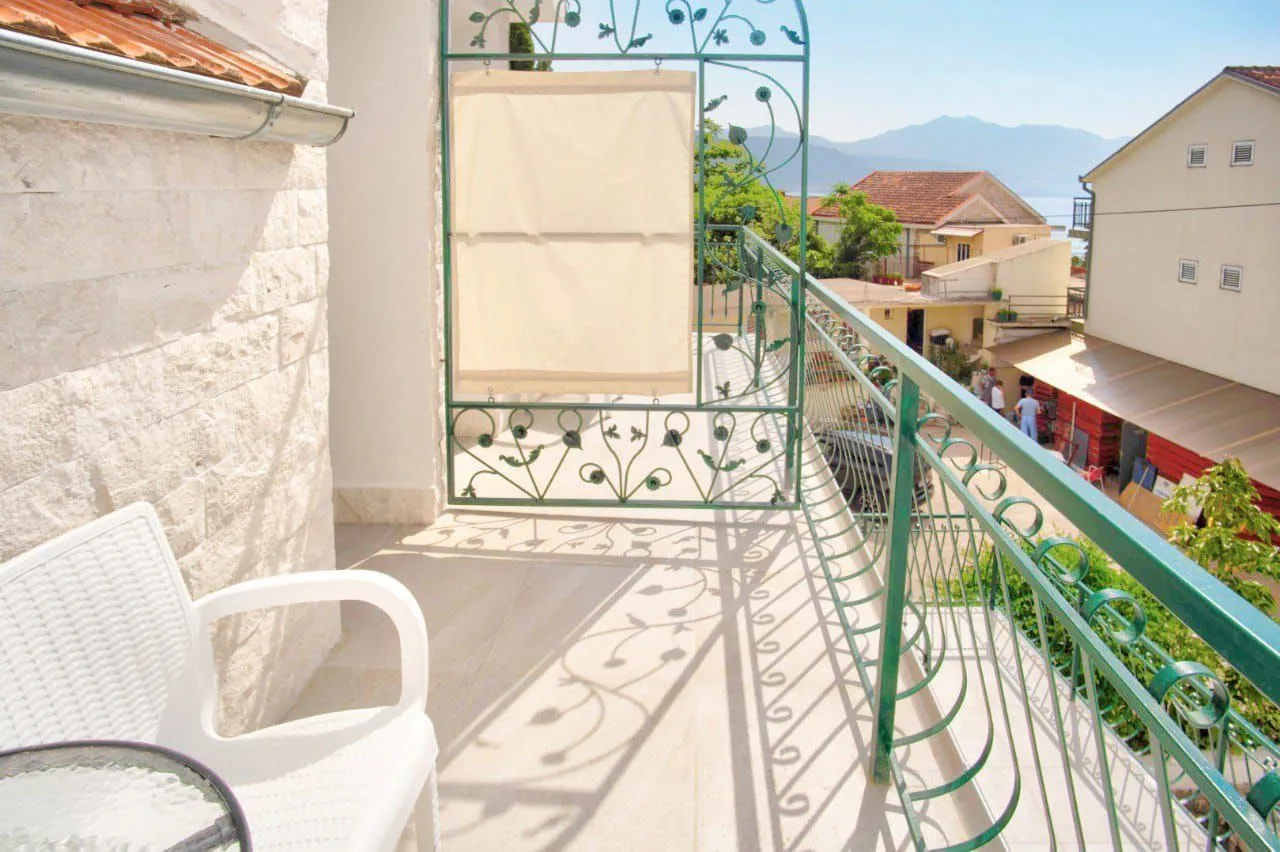 Dugački balkon sa ukrasnom metalnom ogradom i pogledom na okolne kuće i more.