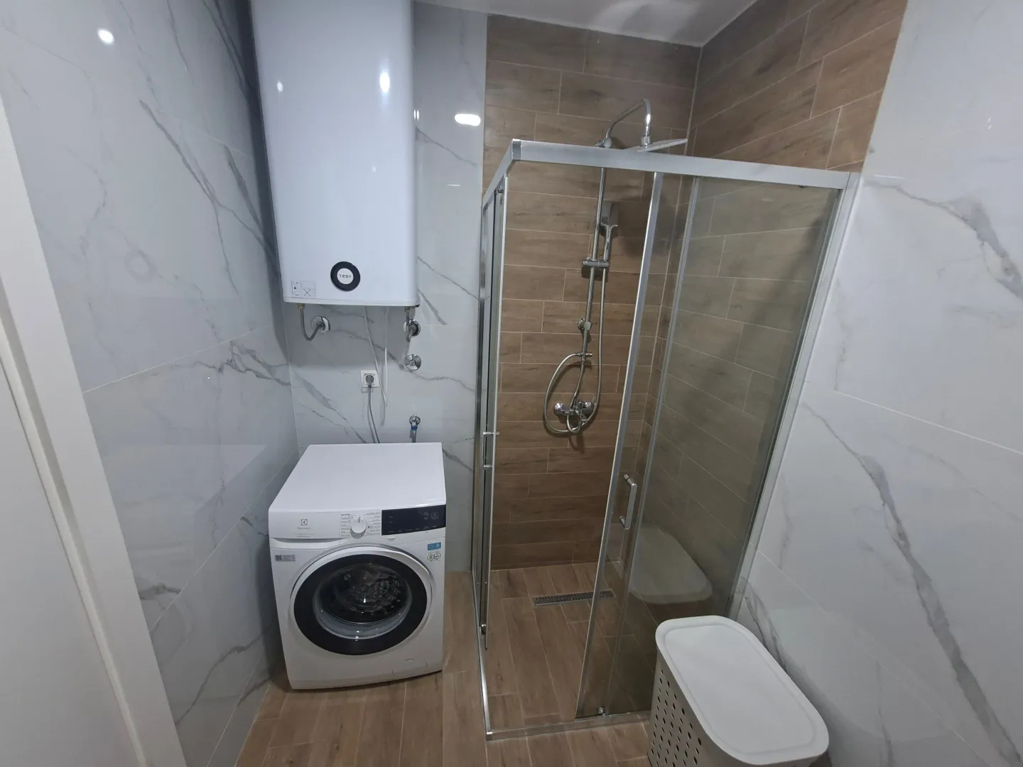 Modern bathroom with a shower cabin, water heater, and washing machine.
