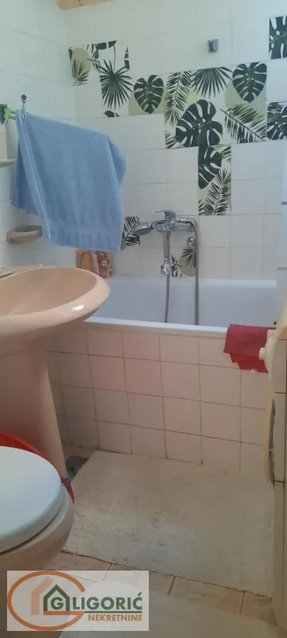 Manje kupatilo sa kadom, umivaonikom i dekorativnim pločicama na zidu.