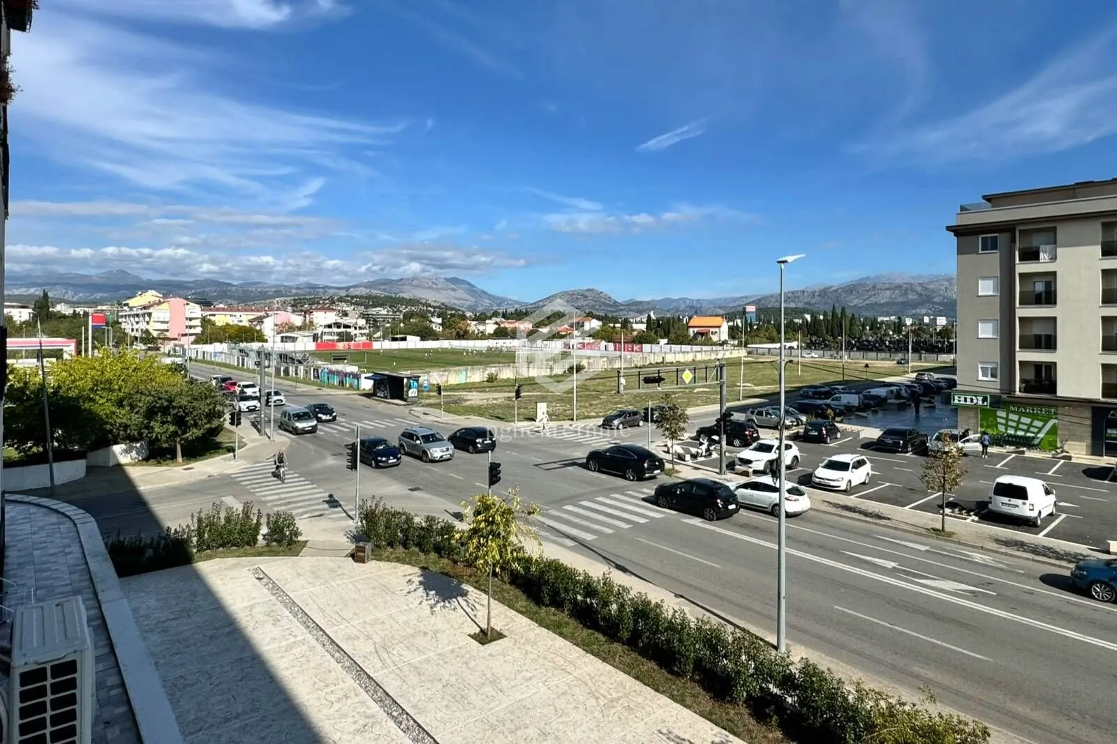 View from the terrace overlooking the city street, parking lot, and surrounding mountains.