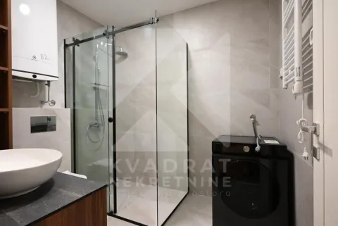 Modern bathroom equipped with a walk-in shower and a black washing machine. - image 3