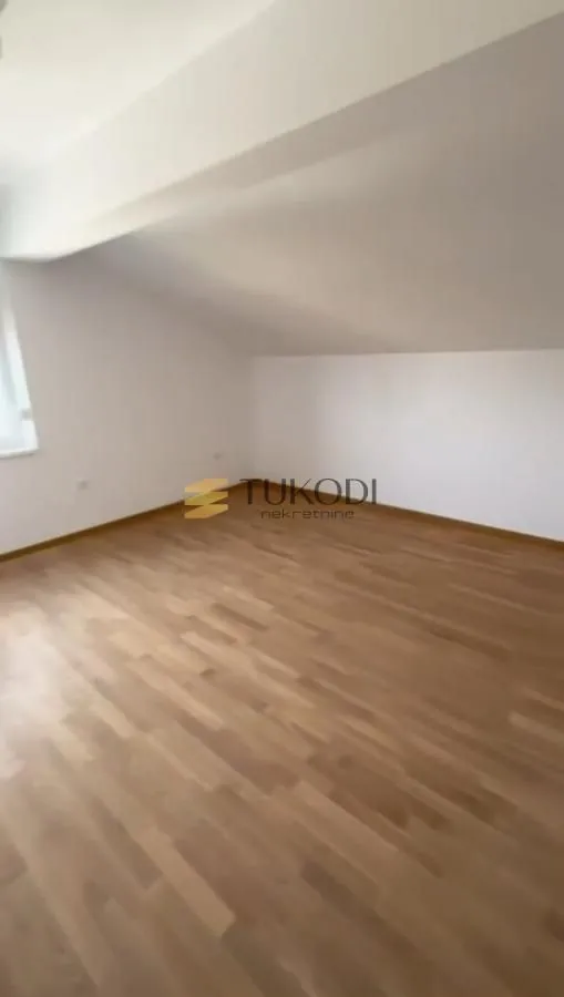Prazna soba sa laminatom i belim zidovima u potkrovlju.